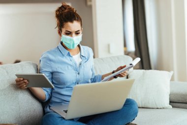 Casual businesswoman with face mask multi-tasking while working at home during coronavirus epidemic. 