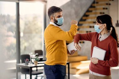 Happy businessman and his female colleague greeting with elbow in the office due to COVID-19 pandemic. 