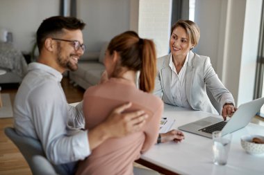 Happy real estate agent using laptop while talking with a couple during the meeting in the office. 