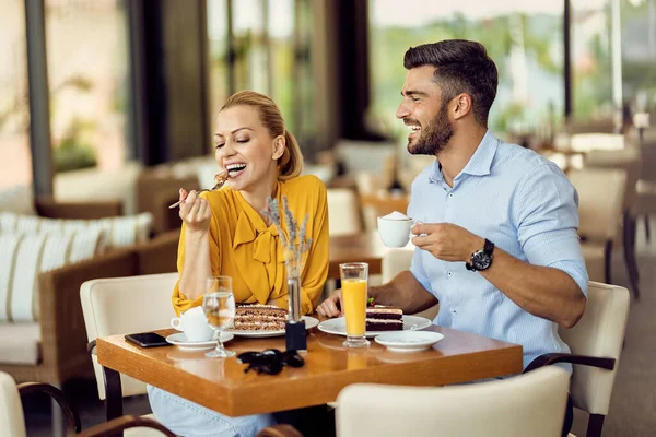 Happy woman enjoying in dessert while her boyfriend is drinking coffee in a cafe.