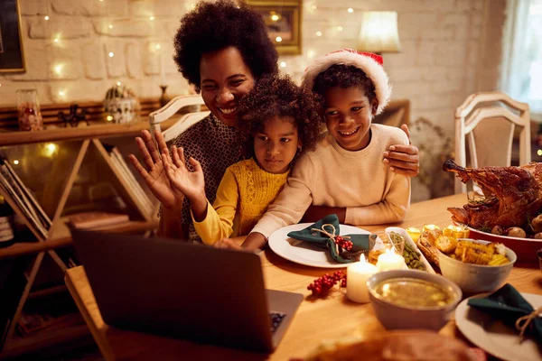 Happy African American children and their mother using laptop and greeting someone via video call on Christmas day.