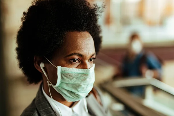 Close-up portrait of black woman with protective face mask in a hallway of public station.