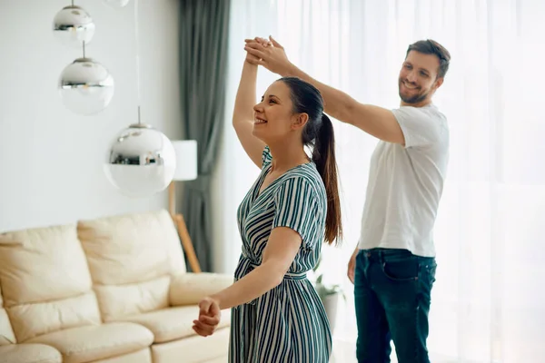 Young happy couple having fun while dancing in the living room.