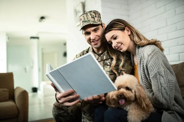 Young happy military couple looking at photo album while reuniting at home.