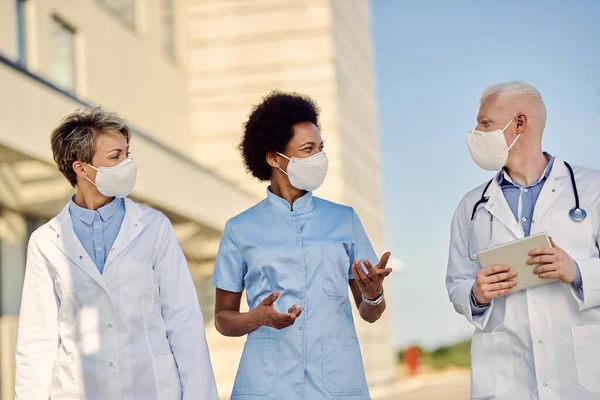 Group of happy healthcare workers wearing face masks while walking outdoor and talking during coronavirus epidemic.