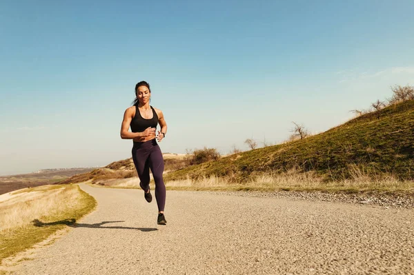 Full length of smiling muscular build sportswoman running on the road. Copy space.