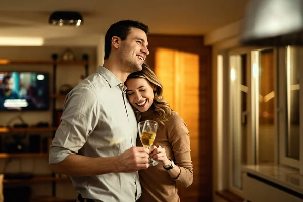 Young couple in love toasting with Champagne while standing embraced in the living room.