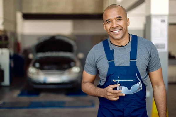 Portrait of happy black mechanic working in auto repair shop and looking at camera.