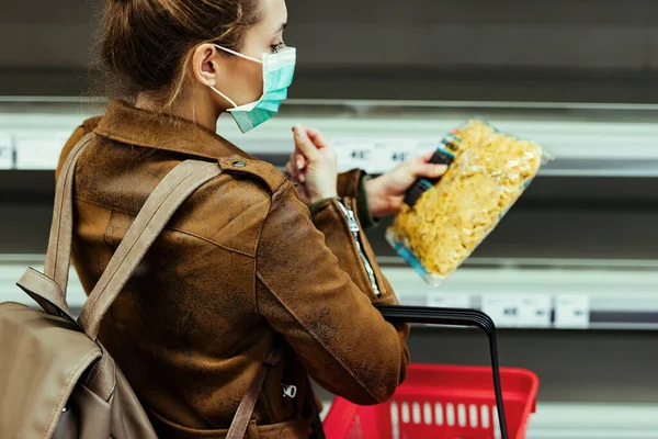 Woman with face mask buying food in grocery store during coronavirus pandemic.