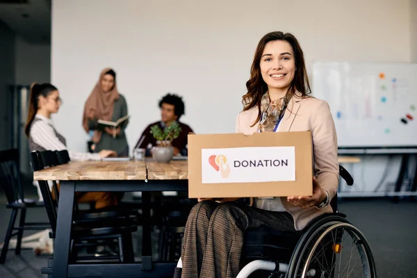 Happy disabled charitable foundation founder holding donation box and looking at camera.