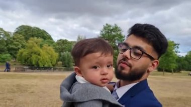 Asyalı Pakistanlı Baba 11 aylık bebeğini İngiltere 'nin Luton kasabasının yerel parkında tutuyor.