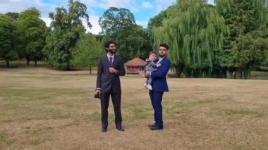 Luton İngiltere 'nin yerel halk parkında 2 Asyalı genç erkek bir bebekle yürüyor.