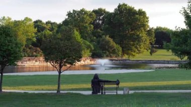 Olathe, Kansas - August, 18 2022 - Statue of Benjamin Franklin taken from behind. The statue is overlooking a small pond on a dark cloudy overcast day
