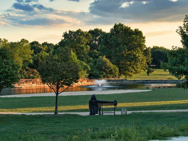 Olathe, Kansas - August, 18 2022 - Statue of Benjamin Franklin taken from behind. The statue is overlooking a small pond on a dark cloudy overcast day