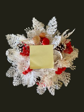 Add text to this close up image of a white wreath on a black background with a yellow sticky note in the center