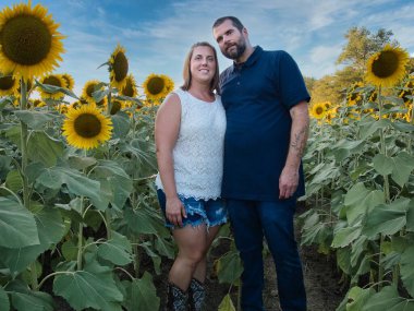 Mavi gömlekli bir adam, güzel bir Lawrence Kansas ayçiçeği tarlasının ortasında dururken beyaz gömlekli bir kadınla poz veriyor.