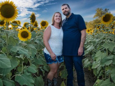 Mavi gömlekli bir adam, güzel bir Lawrence Kansas ayçiçeği tarlasının ortasında dururken beyaz gömlekli bir kadınla poz veriyor.