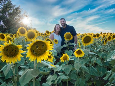 Mavi gömlekli bir adam, güzel bir Lawrence Kansas ayçiçeği tarlasının ortasında dururken beyaz gömlekli bir kadınla poz veriyor.