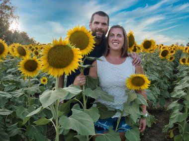 Mavi gömlekli bir adam, güzel bir Lawrence Kansas ayçiçeği tarlasının ortasında dururken beyaz gömlekli bir kadınla poz veriyor.