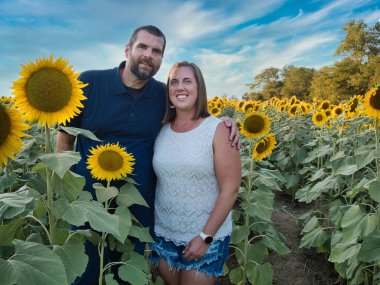 Mavi gömlekli bir adam, güzel bir Lawrence Kansas ayçiçeği tarlasının ortasında dururken beyaz gömlekli bir kadınla poz veriyor.