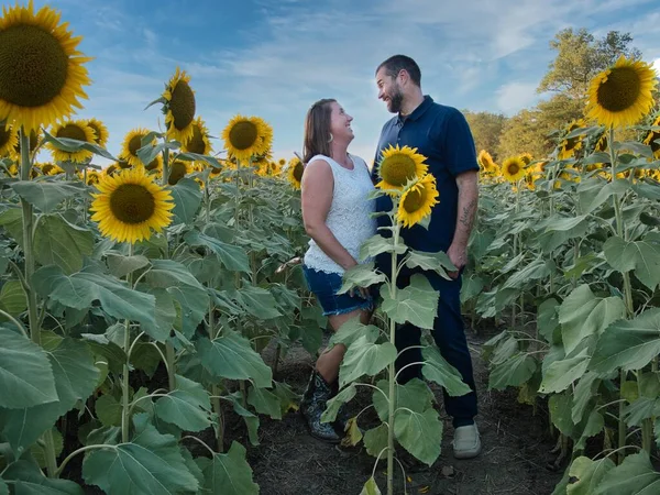 Mavi gömlekli bir adam, güzel bir Lawrence Kansas ayçiçeği tarlasının ortasında dururken beyaz gömlekli bir kadının gözlerinin içine bakıyor.