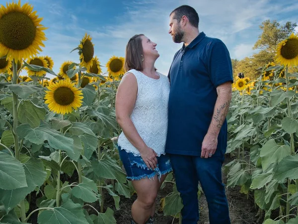 Mavi gömlekli bir adam, güzel bir Lawrence Kansas ayçiçeği tarlasının ortasında dururken beyaz gömlekli bir kadının gözlerinin içine bakıyor.