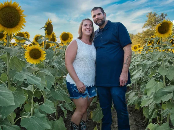 Mavi gömlekli bir adam, güzel bir Lawrence Kansas ayçiçeği tarlasının ortasında dururken beyaz gömlekli bir kadınla poz veriyor.