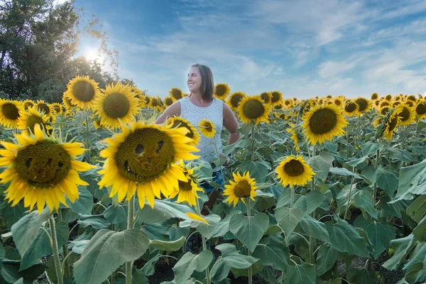Açık kahverengi saçlı ve beyaz gömlekli kadın Lawrence Kansas 'ın dışındaki sarı, yeşil ve kahverengi ayçiçeği tarlasının ortasında duruyor.