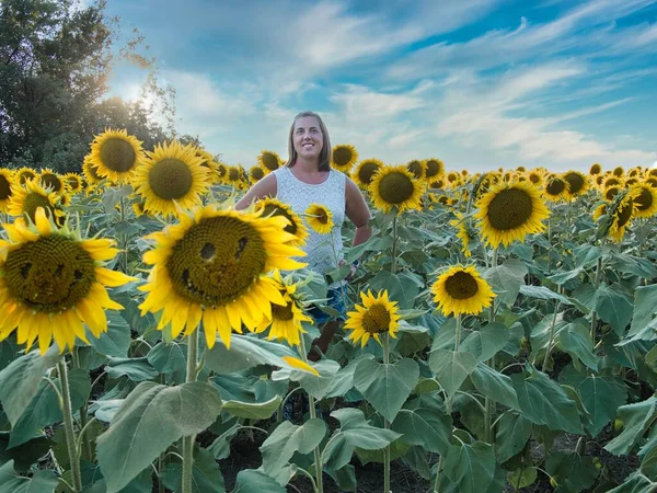 Açık kahverengi saçlı ve beyaz gömlekli kadın Lawrence Kansas 'ın dışındaki sarı, yeşil ve kahverengi ayçiçeği tarlasının ortasında duruyor.