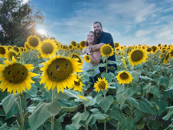 Mavi gömlekli bir adam, güzel bir Lawrence Kansas ayçiçeği tarlasının ortasında dururken beyaz gömlekli bir kadına sarılıyor.