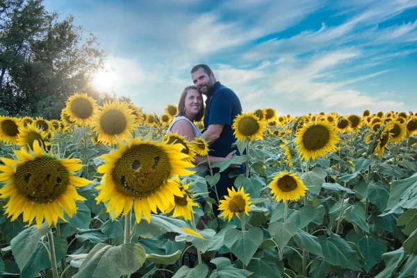 Mavi gömlekli bir adam, güzel bir Lawrence Kansas ayçiçeği tarlasının ortasında dururken beyaz gömlekli bir kadına sarılıyor.