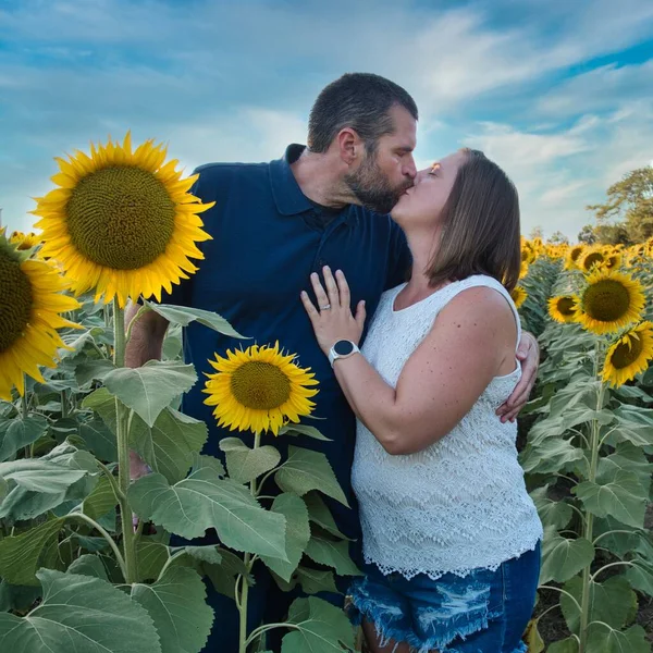 Man in blue shirt kissing a woman in a white shirt while standing in the middle of a beautiful Lawrence Kansas sunflower field