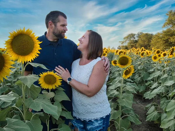 Man in blue shirt gazing into the eyes of a woman in a white shirt while standing in the middle of a beautiful Lawrence Kansas sunflower field