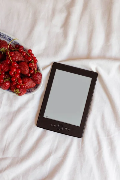 e-book in girl's hands on sheets. fresh berries. cozy atmosphere. life style