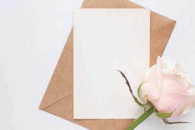 Minimalistic card mockup with roses. craft envelope, white flowers, branches, flat lay, top view. wedding invitation