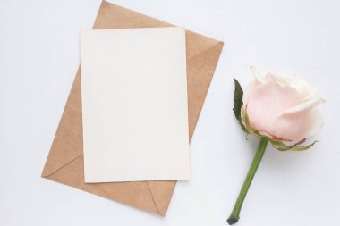 Minimalistic card mockup with roses. craft envelope, white flowers, branches, flat lay, top view. wedding invitation