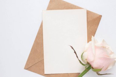 Minimalistic card mockup with roses. craft envelope, white flowers, branches, flat lay, top view. wedding invitation