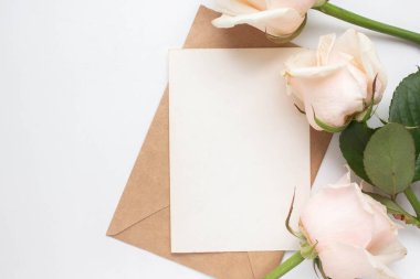Minimalistic card mockup with roses. craft envelope, white flowers, branches, flat lay, top view. wedding invitation