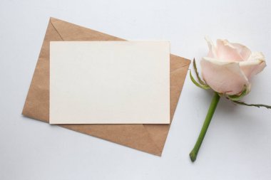 Minimalistic card mockup with roses. craft envelope, white flowers, branches, flat lay, top view. wedding invitation