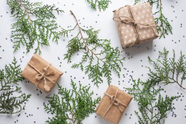 Beyaz masada hediye kutuları ve köknar dalları. Tatil kağıdında kurdele yayı olan bir kutu. Minimalist Noel hediyeleri