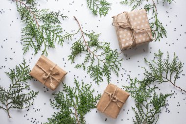 Beyaz masada hediye kutuları ve köknar dalları. Tatil kağıdında kurdele yayı olan bir kutu. Minimalist Noel hediyeleri