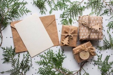 Beyaz masada hediye kutuları ve köknar dalları. Tatil kağıdında kurdele yayı olan bir kutu. Minimalist Noel hediyeleri ve kart modellemeleri