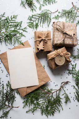 Beyaz masada hediye kutuları ve köknar dalları. Tatil kağıdında kurdele yayı olan bir kutu. Minimalist Noel hediyeleri ve kart modellemeleri