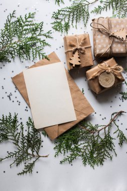 Beyaz masada hediye kutuları ve köknar dalları. Tatil kağıdında kurdele yayı olan bir kutu. Minimalist Noel hediyeleri ve kart modellemeleri