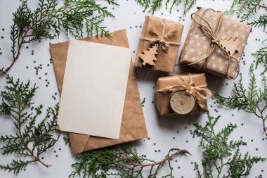 Beyaz masada hediye kutuları ve köknar dalları. Tatil kağıdında kurdele yayı olan bir kutu. Minimalist Noel hediyeleri ve kart modellemeleri
