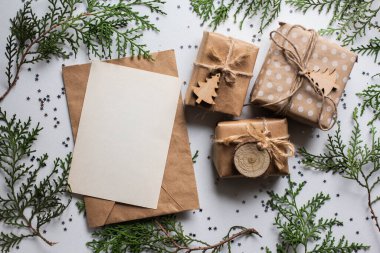 Beyaz masada hediye kutuları ve köknar dalları. Tatil kağıdında kurdele yayı olan bir kutu. Minimalist Noel hediyeleri ve kart modellemeleri