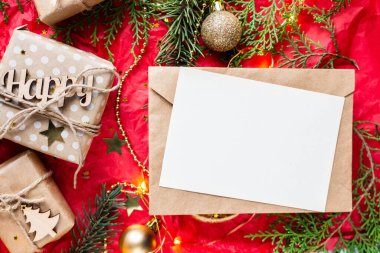 Kırmızı masada hediye kutuları ve köknar dalları. Tatil kağıdında kurdele yayı olan bir kutu. Minimalist Noel hediyeleri, balolar ve kart modellemeleri.