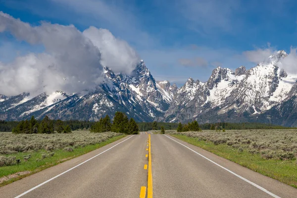 Otoyol, Wyoming 'deki Grand Teton Ulusal Parkı' ndaki dramatik bulutlarla mavi gökyüzünün altındaki Teton Dağları 'nın yüksek, karlı zirvelerini gösteriyordu.