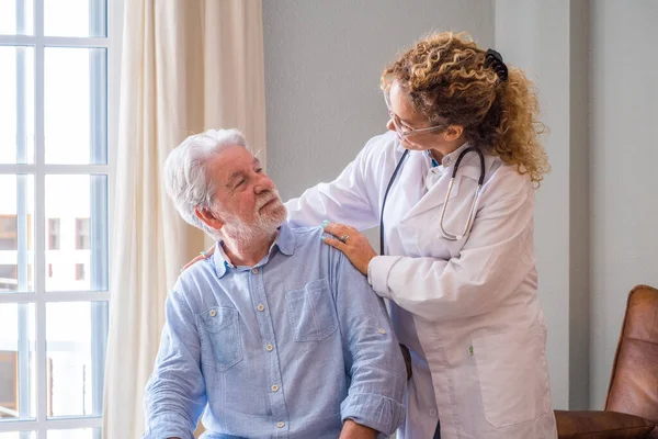 Young female doctor encouraging senior man at home. Doctor helping senior patient and giving care. Female home caregiver taking care of retired old man. Old man and physician talking at nursing home