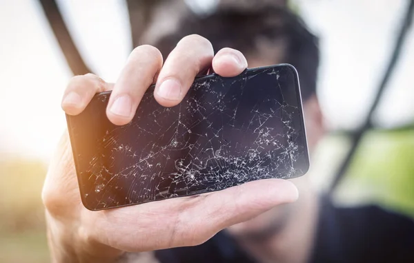Açık havada akıllı telefonu kırılmış bir adam. Erkek el ele tutuşurken cep telefonu dışarıda parçalanmış. Birçok çatlak ve küçük cam parçalarıyla LCD dokunmatik ekran. Ön manzara, kapatma, telefon tamir konsepti..